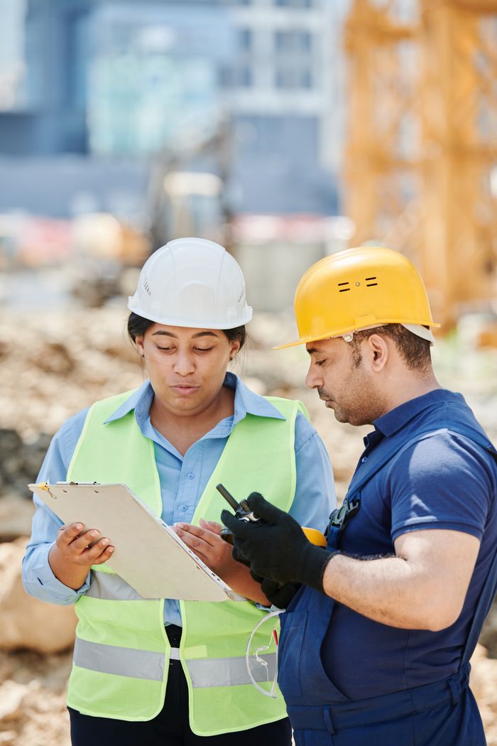 Two construction workers discussing a project on-site, wearing safety gear including hard hats and reflective vests.